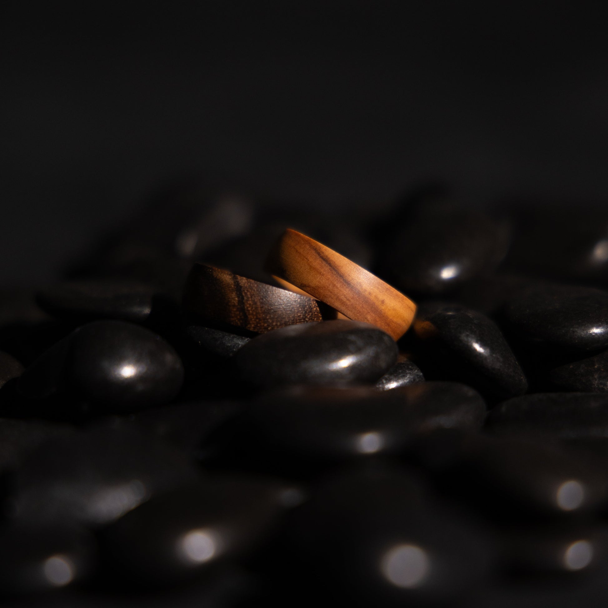 LinkRing Balance olive wood and sandalwood laid on top of each other on a pile of black pebbles