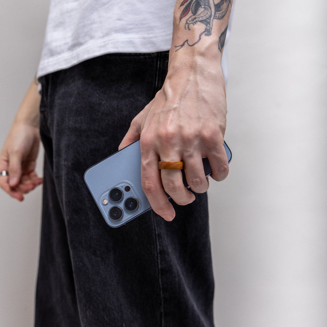 LinkRing Balance Olive Wood Lookbook photo, worn by a male model holding a bright blue Apple iPhone, wearing black jeans and a white T shirt, shot on a bright grey background